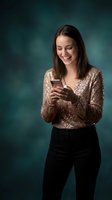 Happy young Caucasian woman in sequined top texting on smartphone against teal background for social media and communication concepts.