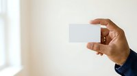 Hand holding blank white business card against neutral background, ready for branding and corporate identity design projects.