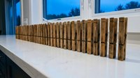 Row of wooden clothespins arranged on white surface near window with blue sky view for laundry organization and household storage solutions.