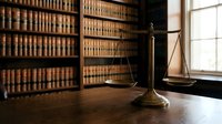 Classic brass scales of justice on wooden desk in traditional law library with vintage legal books for attorney office decor and legal consultation services.