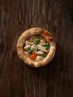 Homemade chicken pot pie with flaky golden crust, tender meat chunks, fresh peas and carrots in creamy sauce on rustic wooden background. Comfort food served hot.