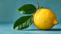 Fresh yellow lemon with green leaves on turquoise background, showcasing vibrant citrus fruit for food and beverage concepts.