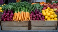 Fresh organic produce in wooden crates at farmers market including vibrant carrots, purple beets, and yellow lemons arranged for retail display.