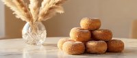 Fresh homemade donuts with golden sugar coating stacked on wooden table with pampas grass decoration in warm natural light for bakery and food photography.