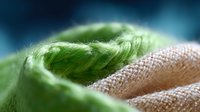 Soft focus macro photography of natural linen fabric and green feather texture creating abstract artistic composition with blurred background.