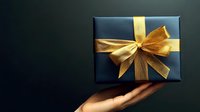 Dark gift box with golden ribbon bow held in cupped hands against black background for holiday celebrations and special occasions.
