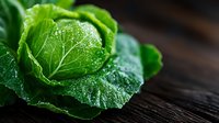 Fresh green cabbage leaf with water drops on dark wooden background, macro shot highlighting natural texture and veins in dramatic lighting.