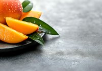 Fresh juicy orange slices with water drops and green leaves on dark plate against grey concrete background, copy space for healthy food design.