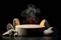 Round stone bowl with rising steam surrounded by natural river rocks on dark background, warm dramatic lighting creates mystical spa atmosphere.