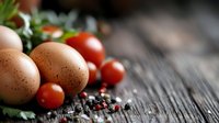 Fresh organic eggs and cherry tomatoes with herbs on rustic wooden table for healthy cooking and farm-to-table cuisine preparation.