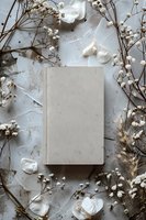 Blank white book cover mockup surrounded by delicate dried baby's breath flowers and white petals on light textured background for elegant product presentation.