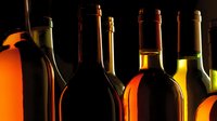 Assorted wine bottles in dramatic lighting showcasing rich amber, red, and golden hues against dark background, creating elegant atmosphere for wine tasting or collection.