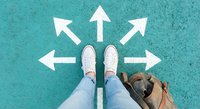 Person standing at crossroads with white directional arrows on turquoise ground, decision making concept for business and life choices.
