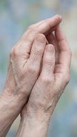 Elderly hands cupped together in protective gesture showing wrinkled skin and age spots against soft blurred background for healthcare concepts.