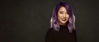 Young Asian woman with vibrant purple hair smiling confidently in black turtleneck against dark background for fashion and beauty concepts.