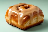 Glazed cinnamon roll with white icing dripping down golden brown pastry on mint green background for bakery menu and dessert advertising.
