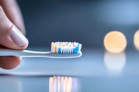 Close-up of toothbrush with colorful toothpaste held by fingers against blurred background with bokeh lights, dental hygiene and oral care concept.