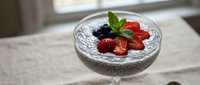 Chia seed pudding topped with fresh strawberries and blueberries, garnished with mint leaf in a glass bowl for healthy dessert recipes.