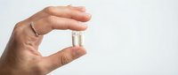 Hand holding white medical pill capsule between fingers on clean background for healthcare and pharmaceutical concepts.