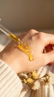 Golden facial serum being applied to woman's hand with glass dropper for natural skincare routine and beauty treatment.