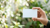 Hand holding blank white card against blurred green foliage background. Suitable for business cards, marketing materials, and promotional designs.