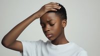 Young African woman with short natural hair and white t-shirt touching head with closed eyes, expressing stress, anxiety or headache against light background.