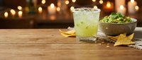 Refreshing lime cocktail with ice served on wooden table beside festive gold star decorations and holiday greenery with warm bokeh lights.
