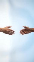 Two hands reaching toward each other against bright sky background symbolizing connection, partnership, teamwork, help, support, unity and cooperation.