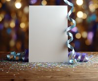 Blank white paper card mockup with blue ribbons and glitter confetti on wooden table against blurred festive bokeh lights background for celebration design.