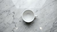 Empty white ceramic cup on marble surface, overhead view, minimalist tabletop styling for beverage, kitchen, and cafe design projects.