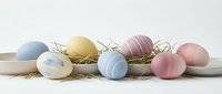 Pastel colored Easter eggs in soft blue, pink and yellow tones arranged with natural straw nest material on white wooden surface for spring holiday decor.