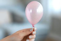 Female hand with white manicure holding small pink balloon against blurred background. Minimalist composition for celebration and party concepts.