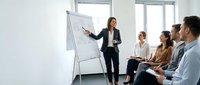 Professional businesswoman presenting strategy on whiteboard to diverse team in modern office meeting room for corporate training and development.