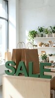 Green SALE letters and kraft paper shopping bags on a wooden counter in a bright eco-friendly retail store with plants.