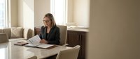 Professional businesswoman working with documents at modern office desk near window with natural lighting for corporate presentations.
