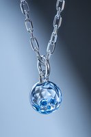 Elegant blue crystal pendant on silver chain against gradient background, featuring faceted spherical gemstone with intricate internal pattern. Luxury jewelry macro.
