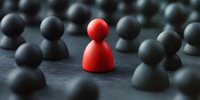 Red figure standing out among black figures on dark surface, representing uniqueness, leadership and individuality in business concept. Selective focus background.