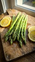 Fresh green asparagus spears with lemon slices and sea salt on rustic wooden cutting board by kitchen window for healthy cooking and meal preparation.