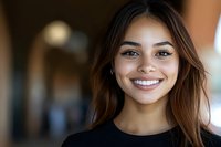 Young woman with long brown hair and warm smile wearing black shirt, indoor portrait with blurred background, suitable for business, lifestyle, and professional content.
