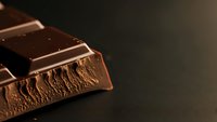Dark chocolate bar pieces with rich cocoa texture on black surface for gourmet food photography and culinary marketing materials.