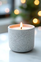 Lit aromatic candle in speckled ceramic holder with soft bokeh lights background creates cozy atmosphere for spa, meditation, or holiday decor.
