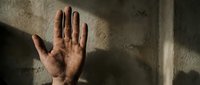 Stop sign gesture by male hand against weathered concrete wall with dramatic shadow lighting for concepts of refusal, halt, rejection, or warning.