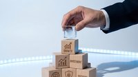 Businessman hand placing glass cube on top of wooden blocks with growth and investment icons, symbolizing financial strategy and business success.