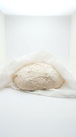 Artisan sourdough bread dough wrapped in parchment paper, ready for baking. Use for bakery, cooking, and food preparation content.