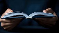 Person holding open book with dramatic lighting against dark background, creating atmospheric mood for education, knowledge, or literary concepts.