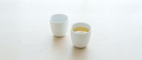 Two white ceramic cups on wooden surface, one filled with golden tea or herbal beverage, minimalist kitchen tableware for morning routine and relaxation.