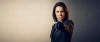 Professional businesswoman in black suit pointing forward with confident gesture against neutral background for corporate presentations.