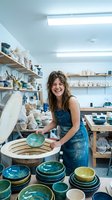 Happy female potter working with ceramic bowl in bright pottery studio workshop surrounded by handmade pottery and art supplies.