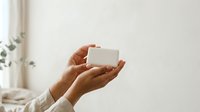 Close-up of hands holding a blank white box against a neutral background, suitable for product packaging mockups, branding presentations, and commercial advertising campaigns.