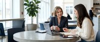 Professional businesswomen having productive meeting in modern office space with laptop and documents discussing corporate strategy and collaboration.